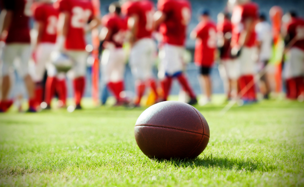 Image of a football on grass with football players blurred in the background